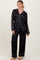woman wearing a black satin pajama set with white piping, featuring long sleeves and wide-leg pants