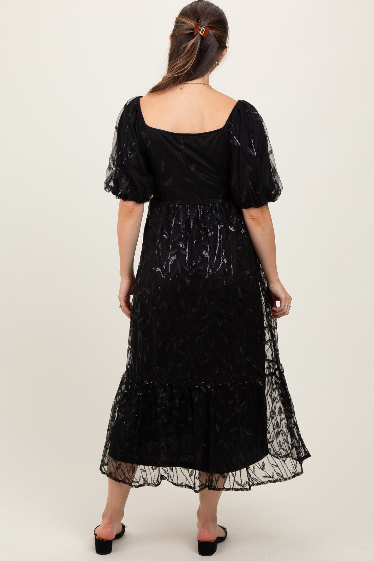 woman wearing a black maternity maxi dress with sheer puff sleeves and a ruffled hem, showing a baby bump from behind