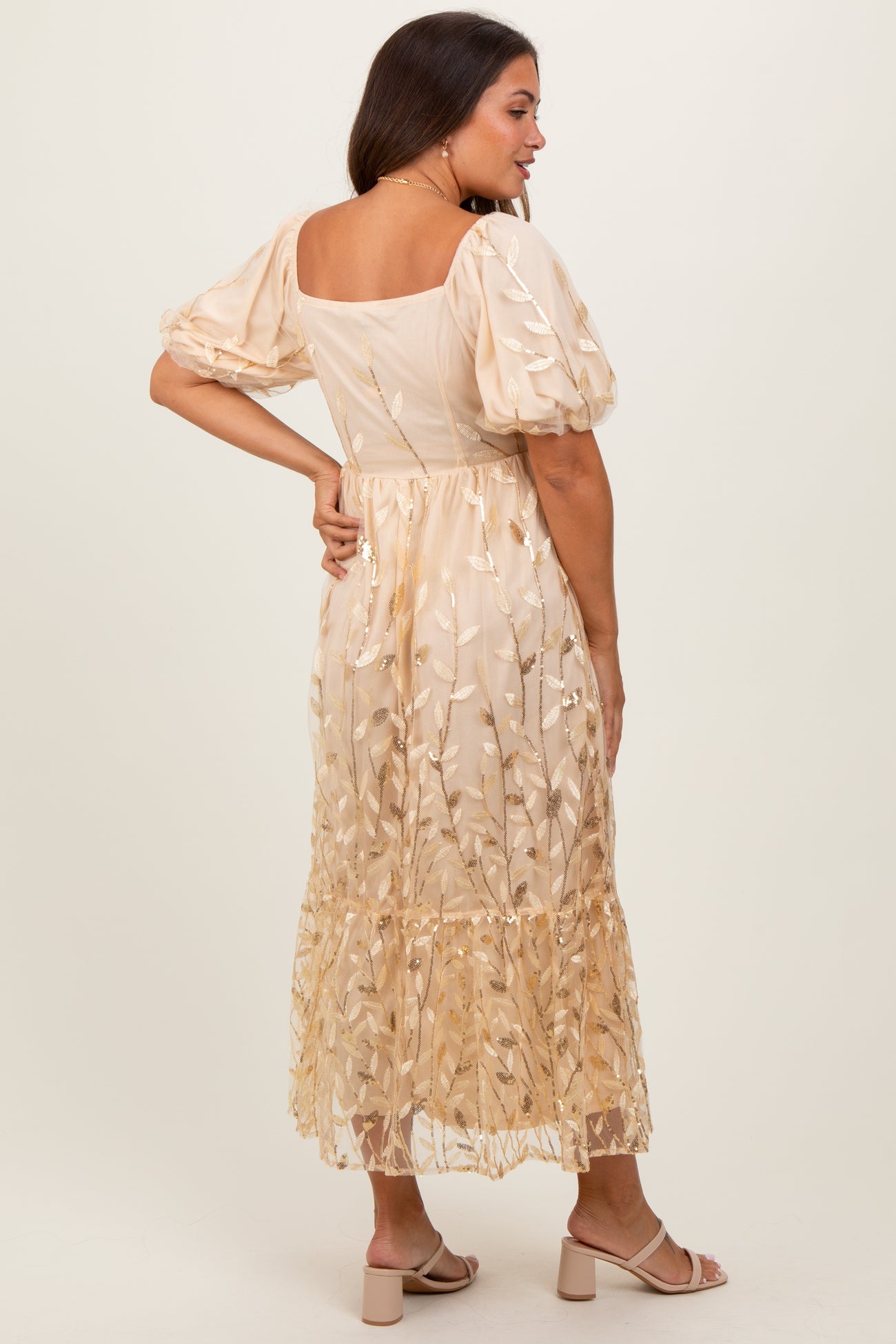 woman wearing a beige maternity dress with puff sleeves and floral embroidery, showing back view