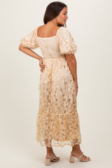 woman wearing a beige maternity dress with puff sleeves and floral embroidery, showing back view