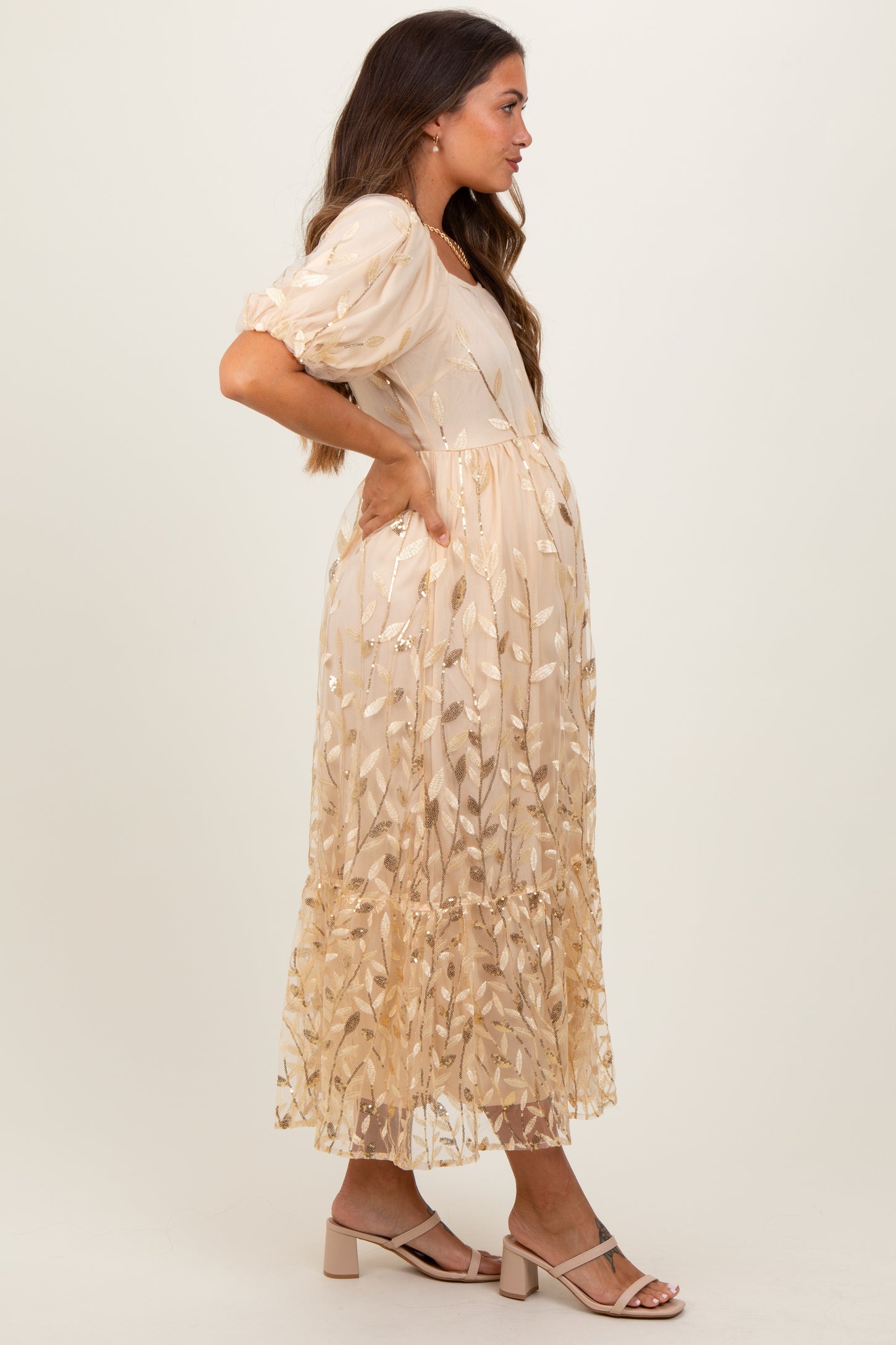 woman wearing a beige maternity dress with floral embroidery, puff sleeves, and a flowing skirt, showing her baby bump
