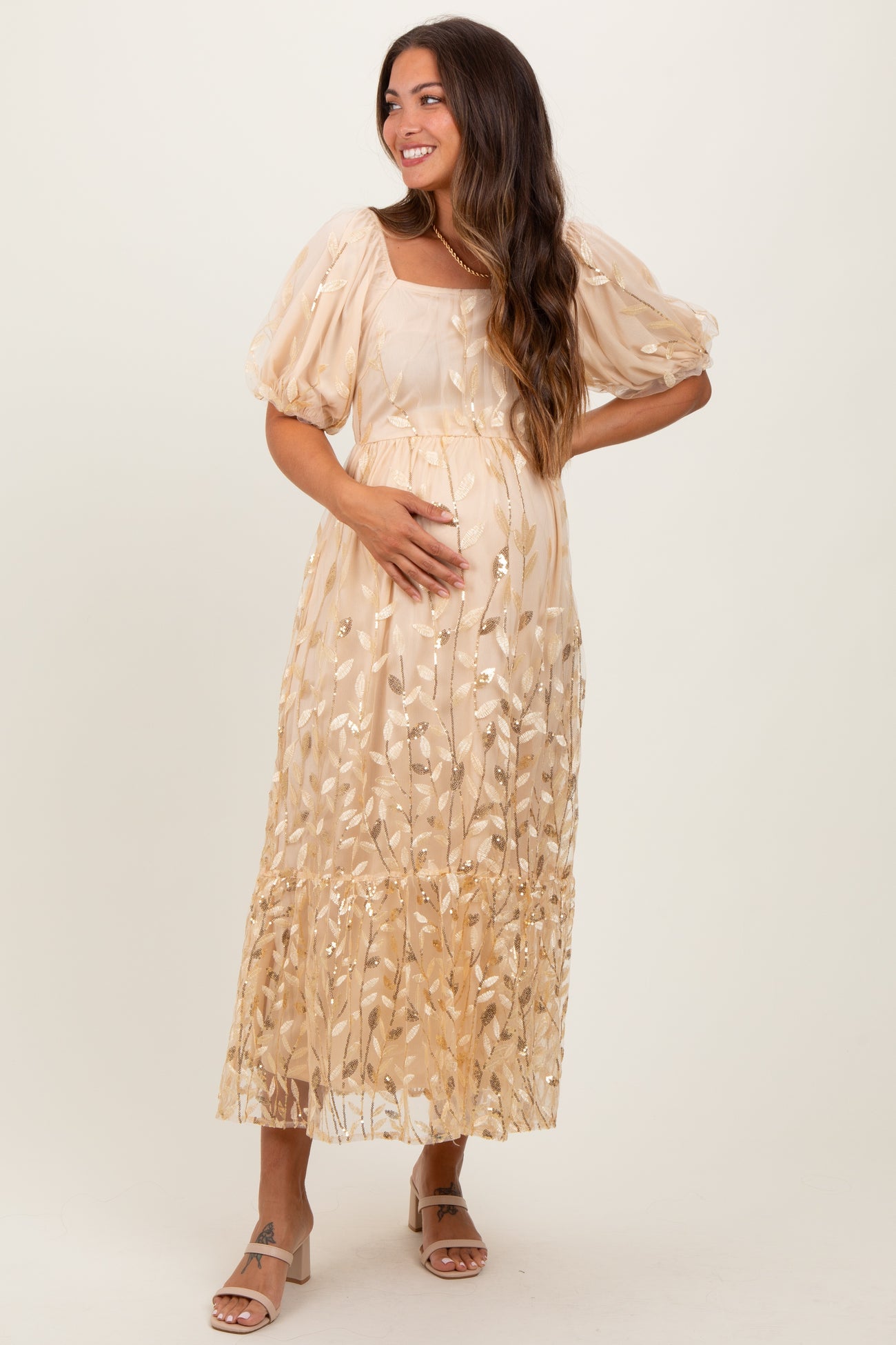 woman wearing a beige maternity maxi dress with floral embroidery and puff sleeves, showing her baby bump