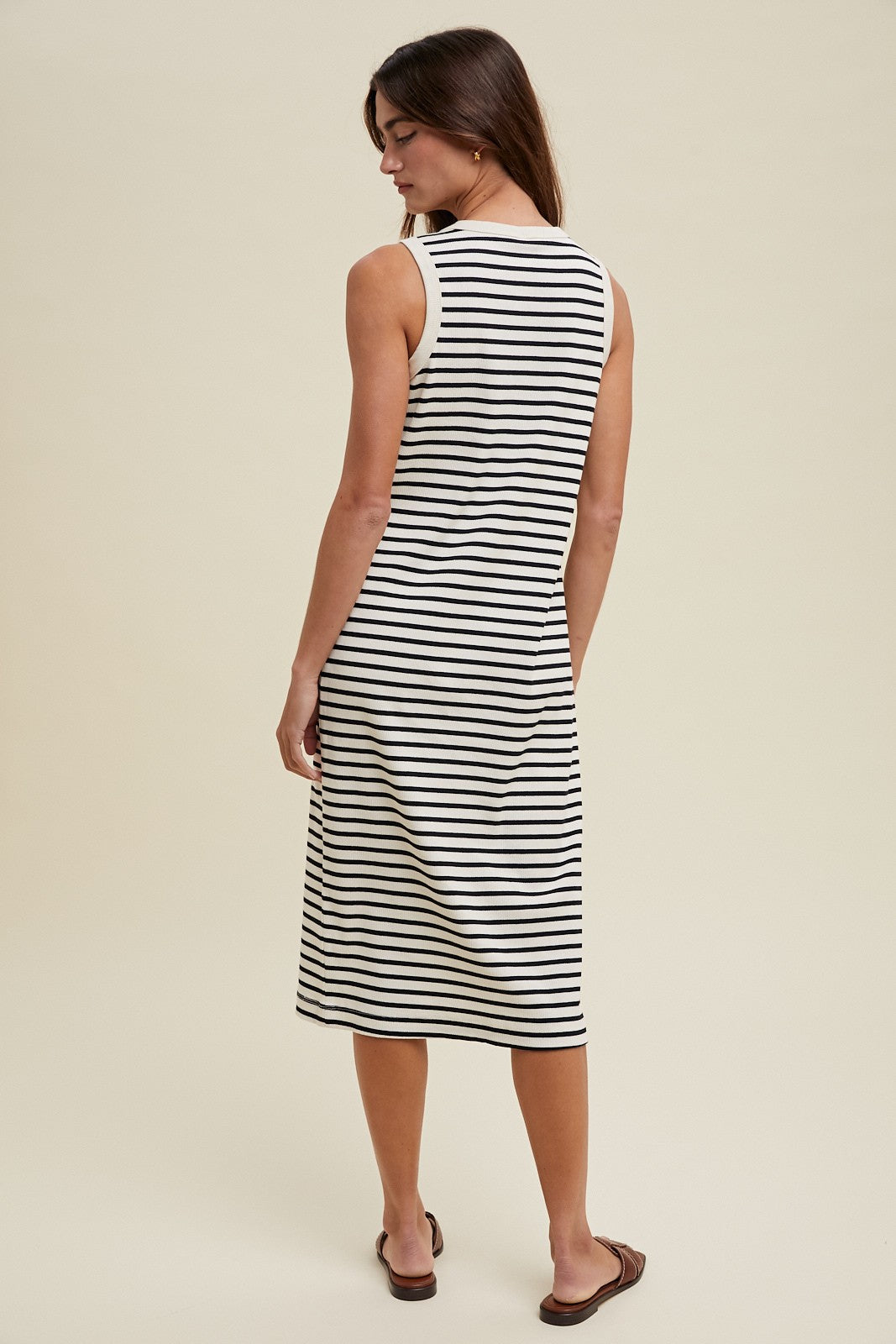 woman wearing a black and white striped sleeveless midi dress, standing with her back to the camera
