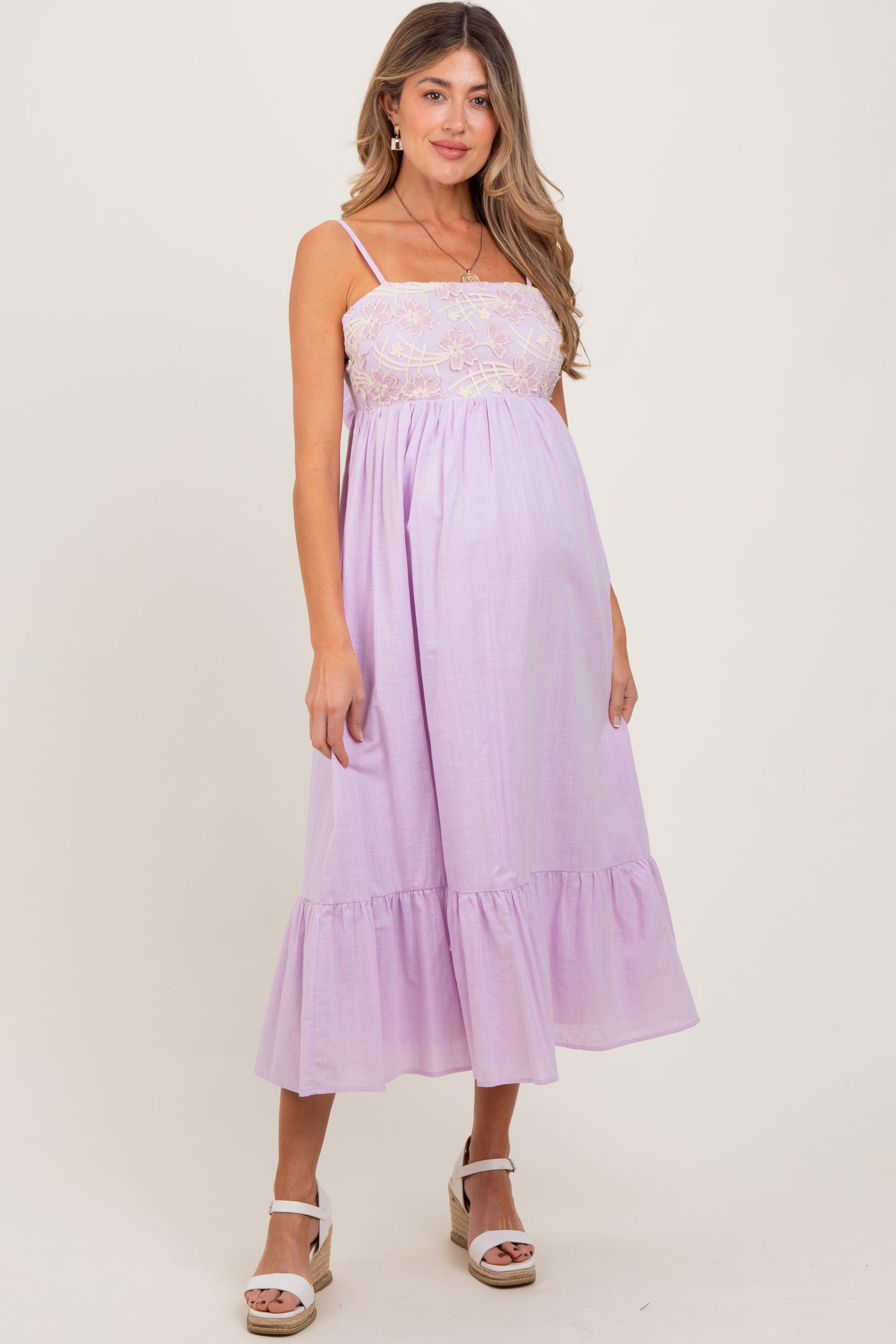 woman wearing a lilac maternity dress with embroidered bodice and ruffled hem, showing her baby bump