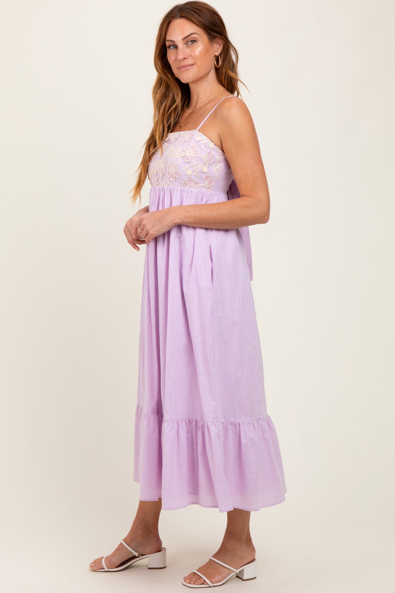 woman wearing a lilac midi dress with lace detailing and a tiered ruffle hem, standing sideways