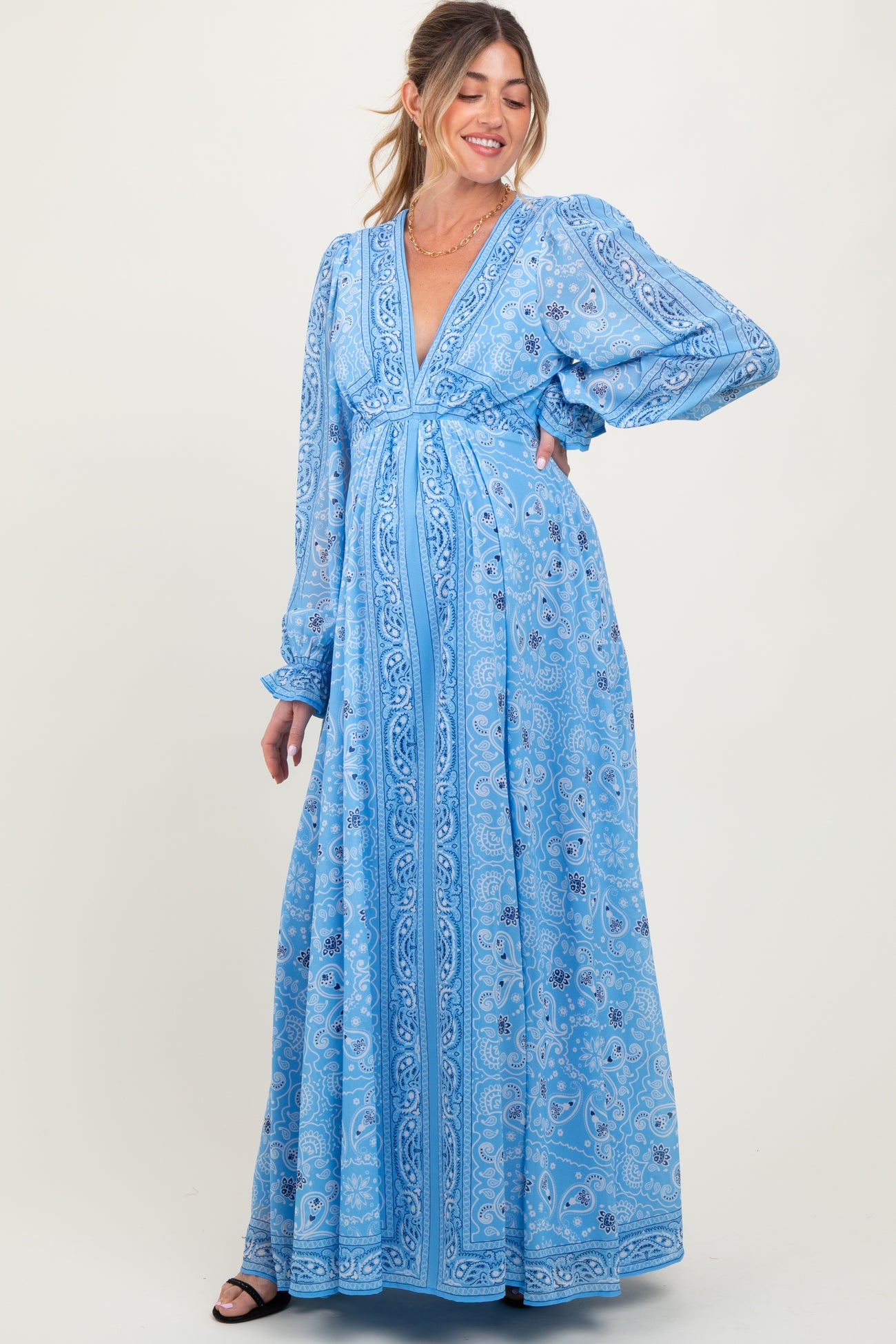 woman wearing a light blue paisley print maternity maxi dress with a v-neckline and long sleeves, showing her baby bump