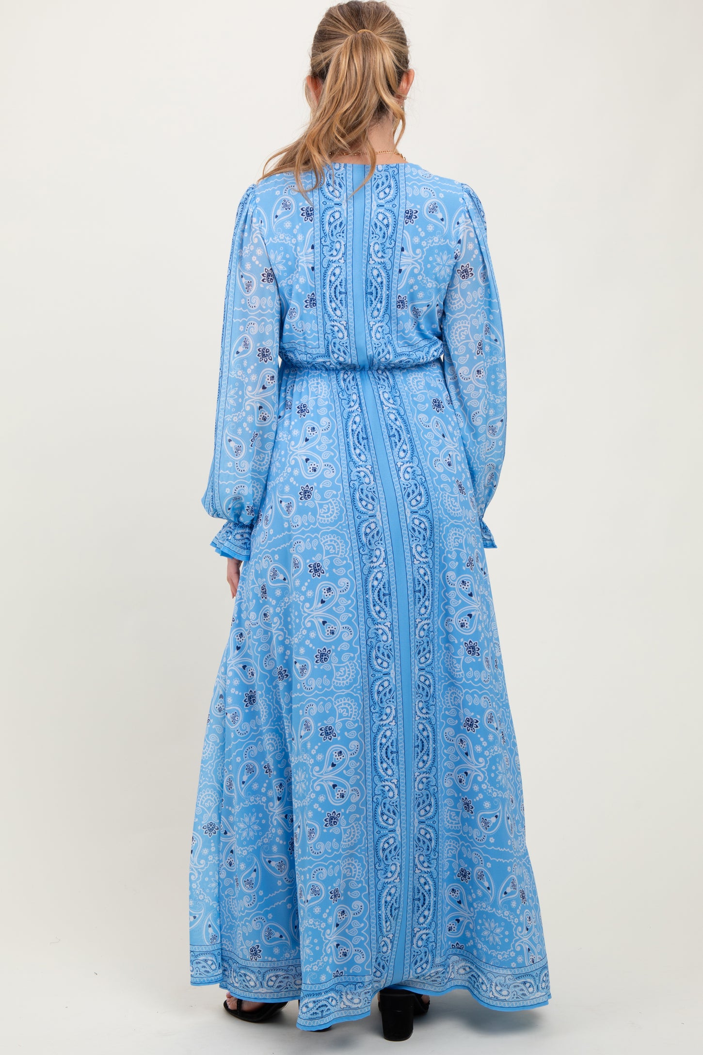 woman wearing a long sleeve blue patterned maternity maxi dress with a tie waist from the back