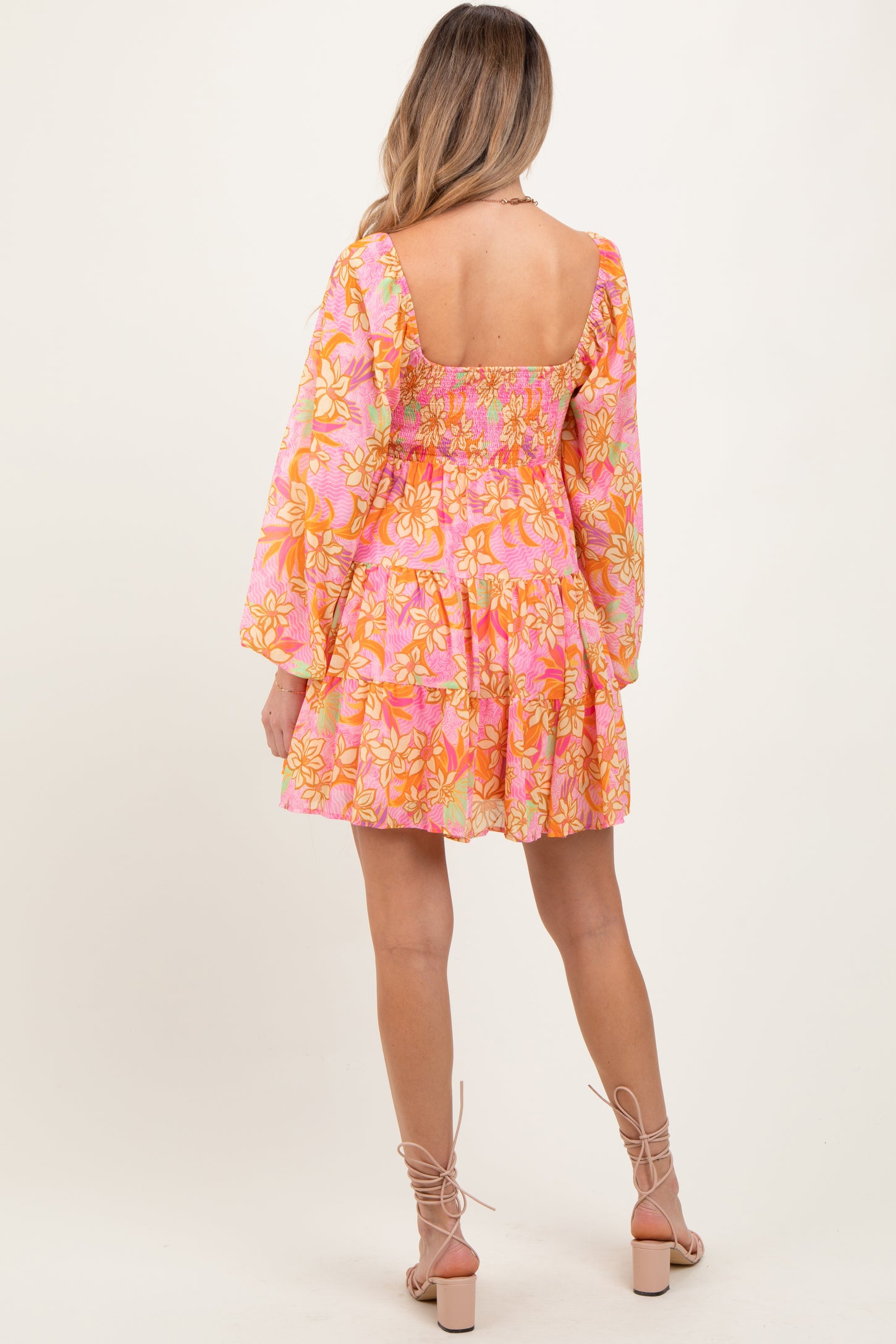 woman wearing a pink floral maternity dress with long sleeves and a tiered skirt, showing a smocked back design