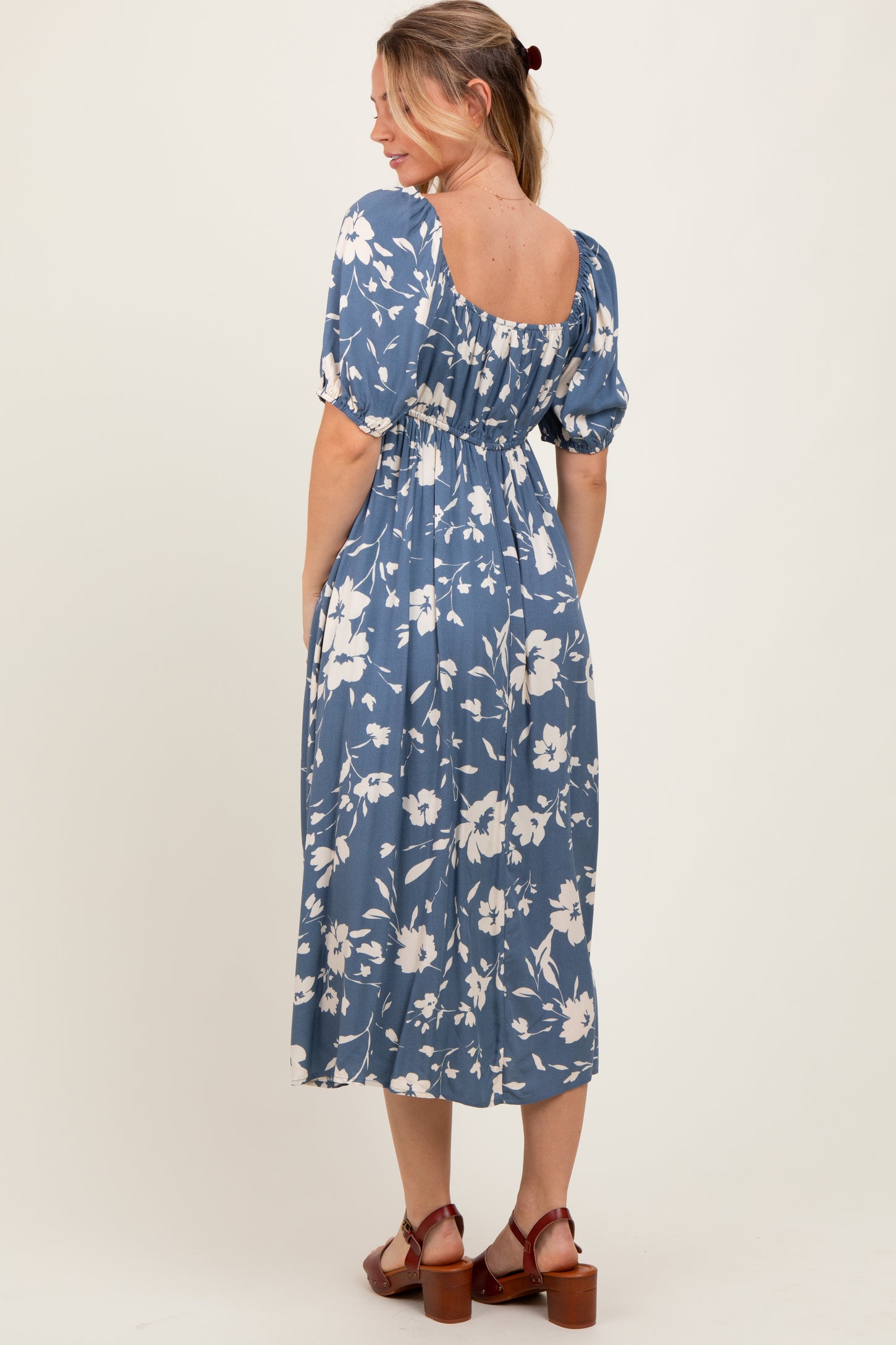 woman wearing a blue floral midi dress with puff sleeves and a smocked back, standing sideways