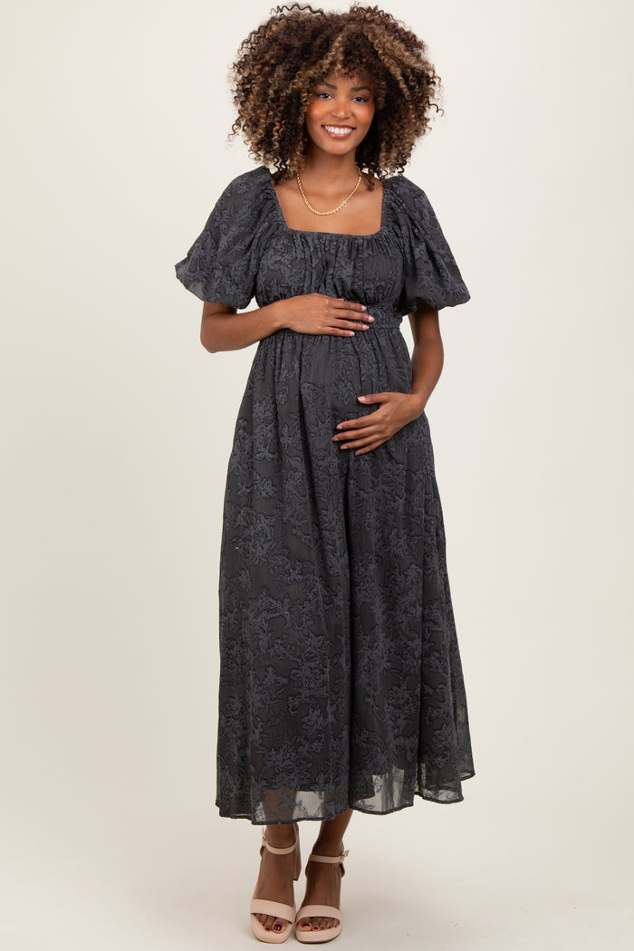 woman wearing a dark gray floral maternity dress with puff sleeves and holding her baby bump