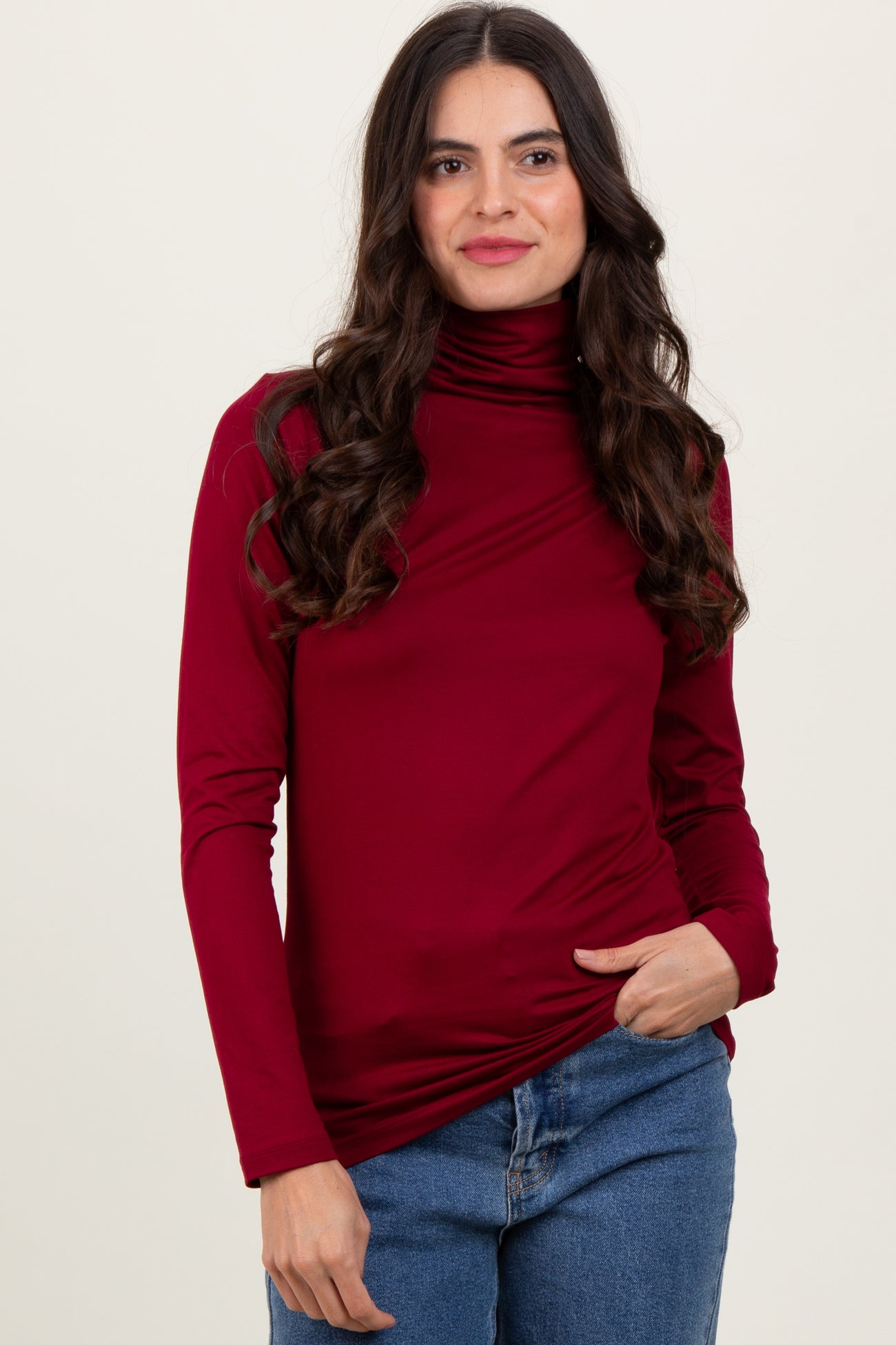 woman wearing a burgundy long sleeve turtleneck top with draped details and styled with blue jeans