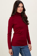 woman wearing a burgundy long sleeve turtleneck top and blue jeans