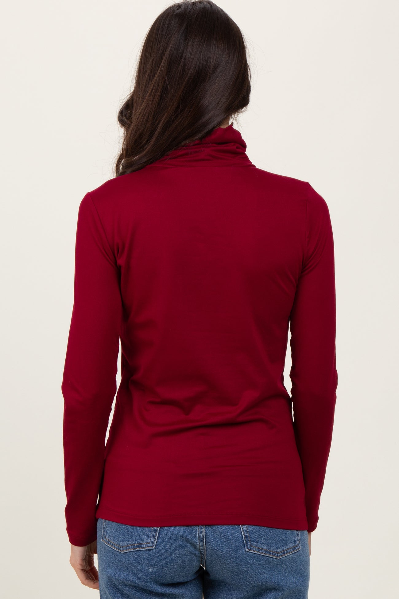 woman wearing a burgundy long sleeve turtleneck top viewed from the back with loose-fitting styling