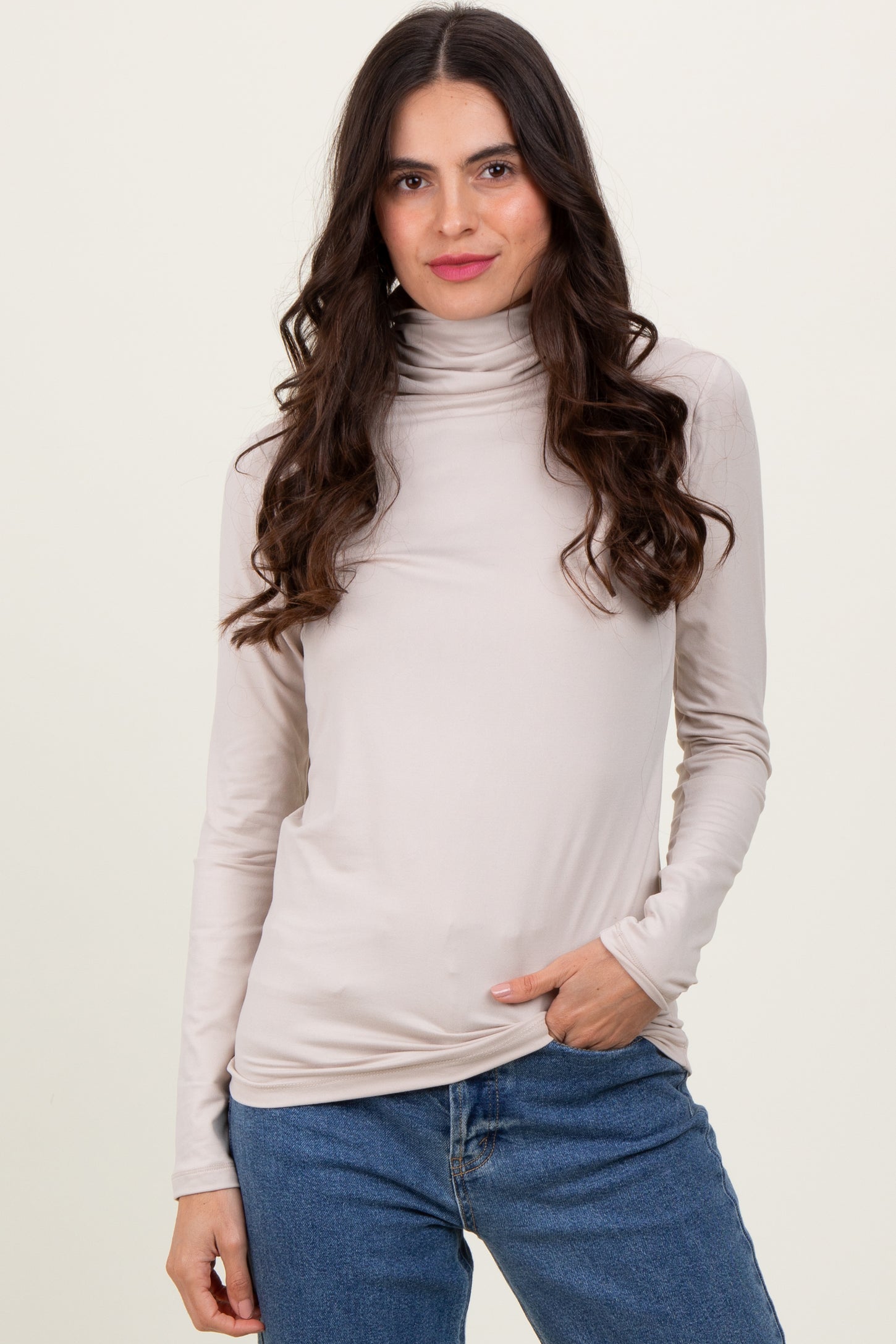 woman wearing a light beige long sleeve turtleneck top with a fitted style and casual jeans