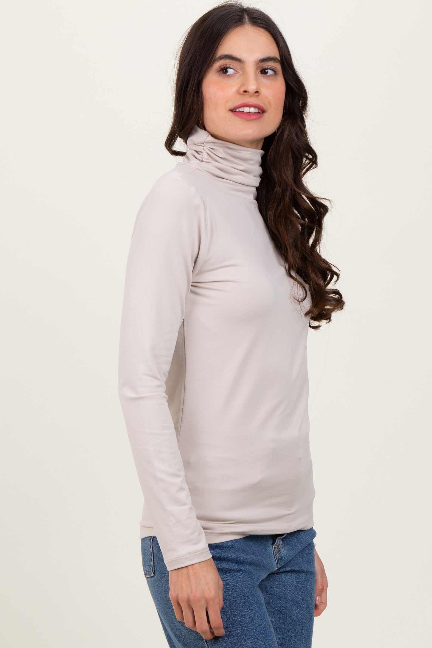 woman wearing a light beige long sleeve turtleneck top and blue jeans