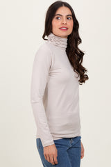 woman wearing a light beige long sleeve turtleneck top and blue jeans