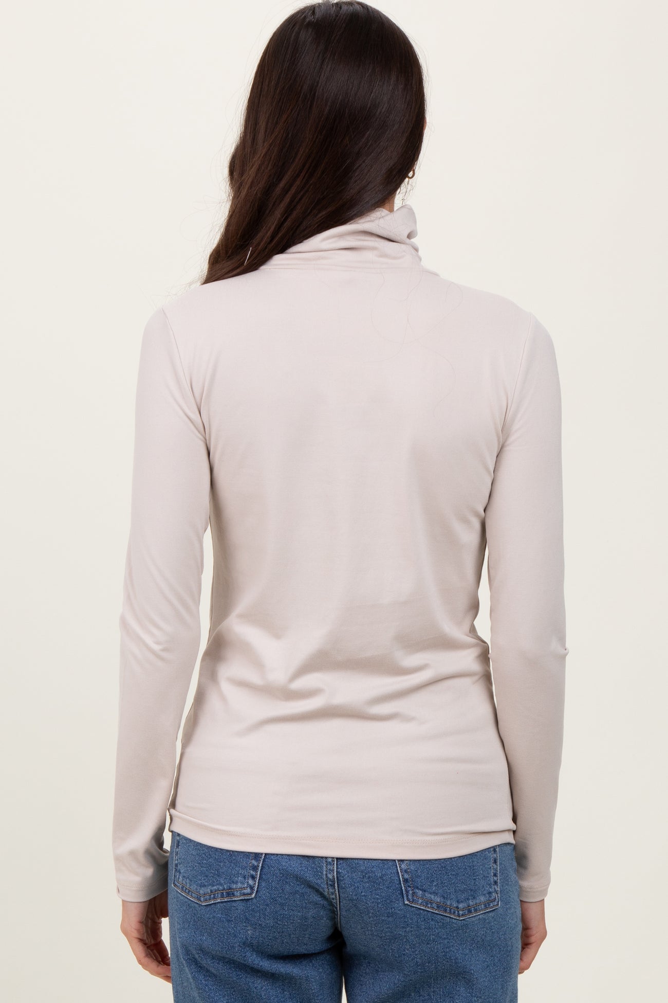 woman wearing a light beige long sleeve mock neck top, viewed from the back with jeans