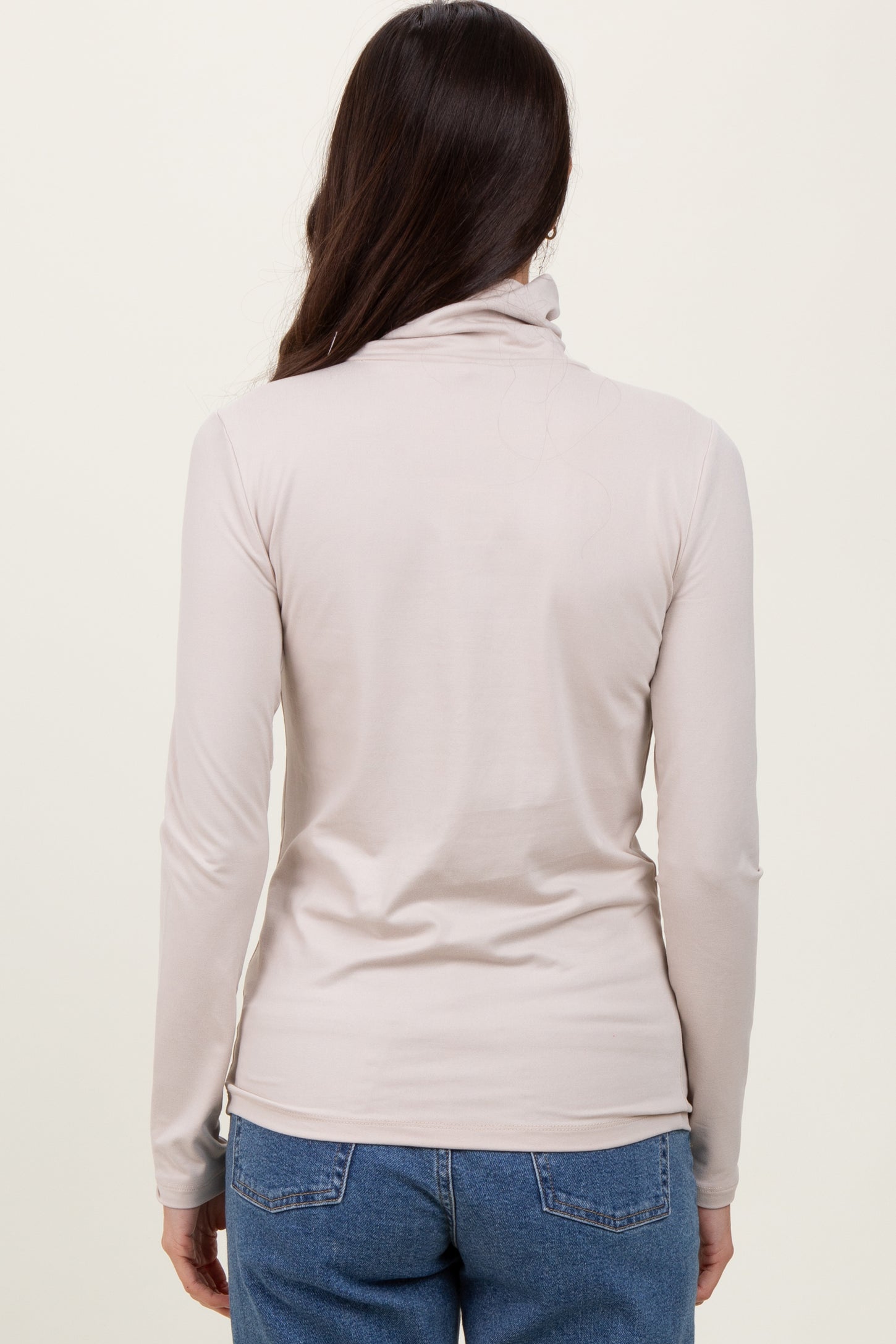 woman wearing a light beige long sleeve mock neck top, viewed from the back with jeans