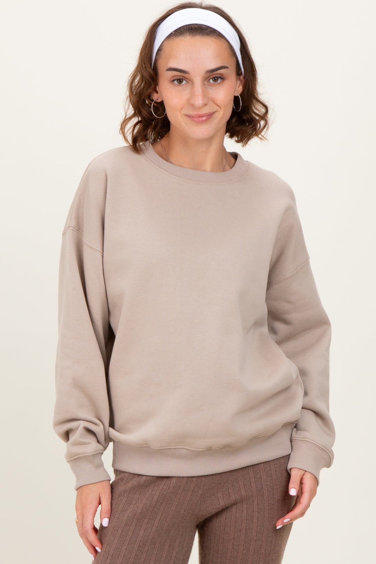 woman wearing a beige oversized sweatshirt with dropped shoulders and a round neckline, paired with brown ribbed pants