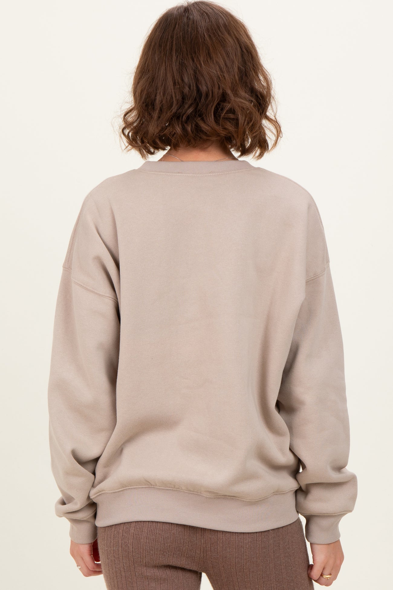 woman wearing a light brown oversized sweatshirt, seen from the back, with ribbed cuffs and hem