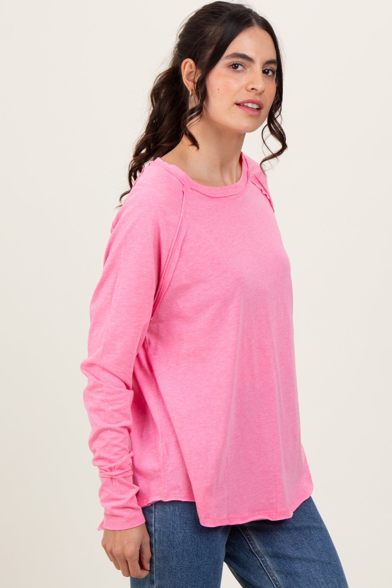 woman wearing a pink long sleeve relaxed fit top with a round neckline and side slits