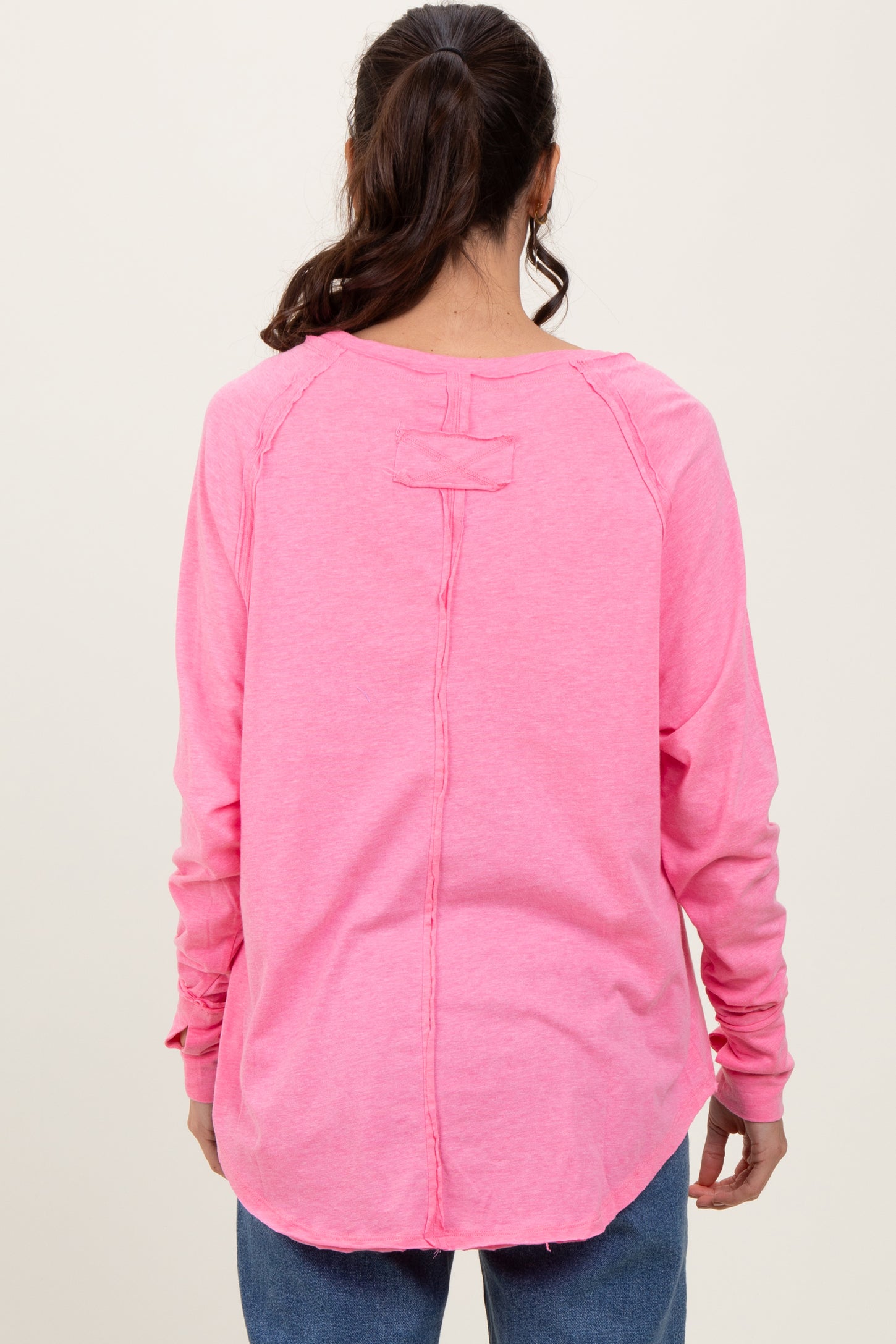 woman wearing a bright pink long sleeve top with a low back and relaxed fit