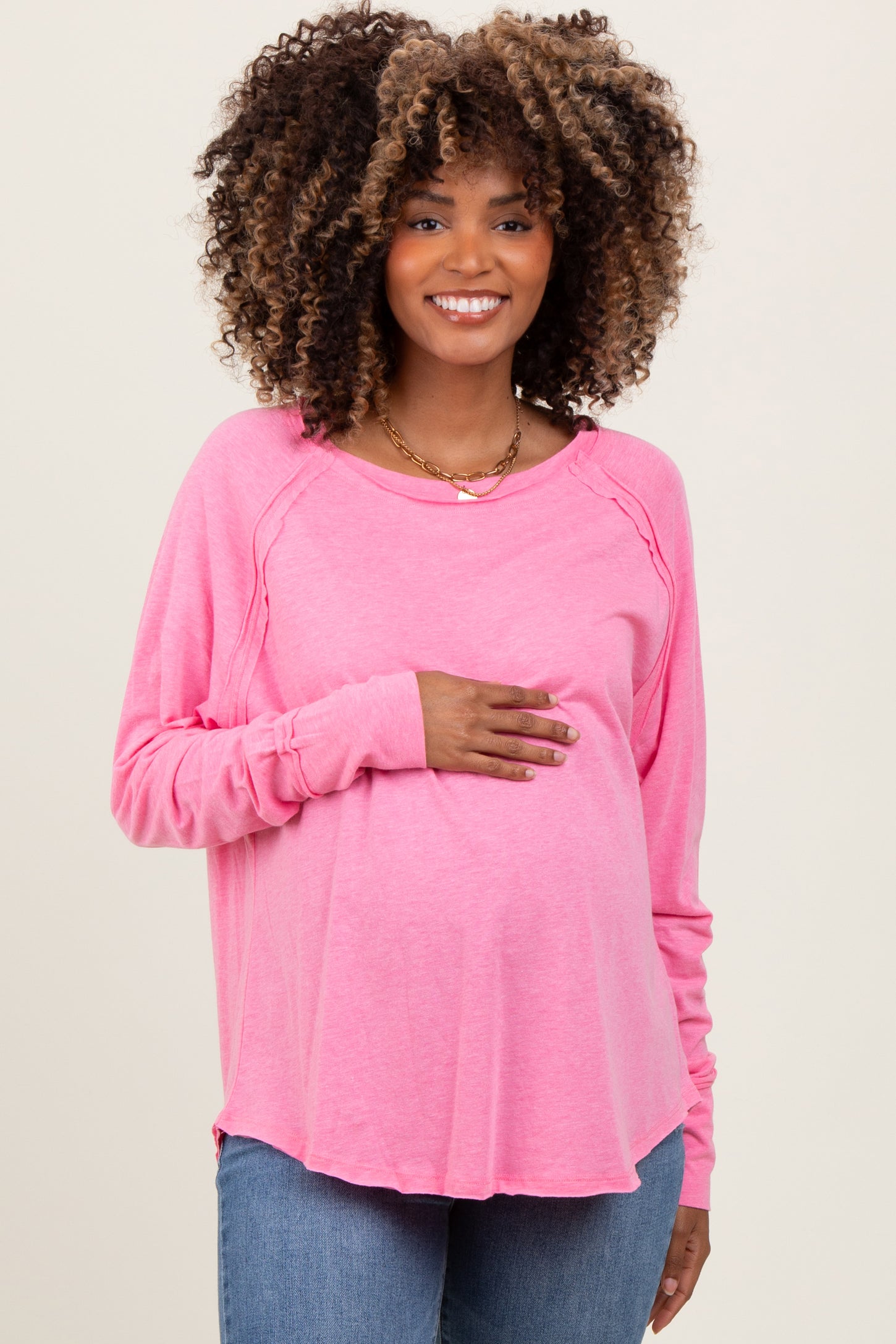 woman wearing a pink long sleeve maternity top and holding her baby bump