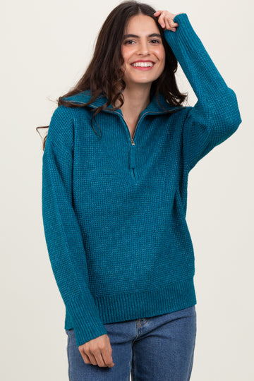 woman wearing a teal zip-up sweater with a textured knit design and a relaxed fit, smiling and posing with one hand in her hair