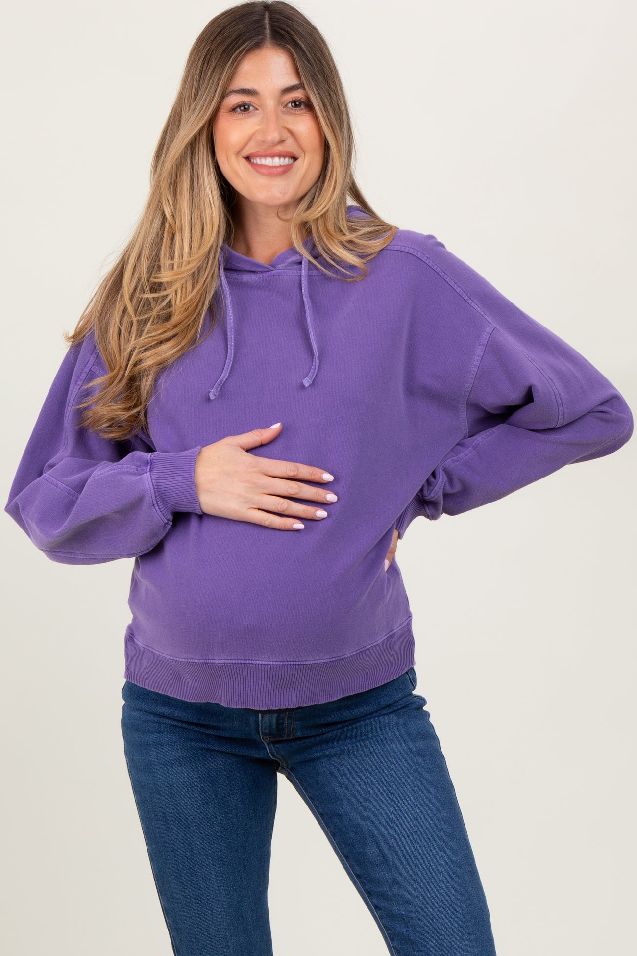 woman wearing a purple maternity sweatshirt and holding her baby bump while smiling