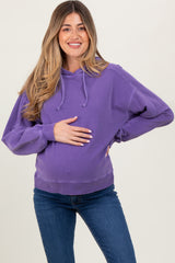 woman wearing a purple maternity sweatshirt and holding her baby bump while smiling