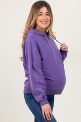 woman wearing a purple hooded sweatshirt, showing her baby bump, paired with blue jeans