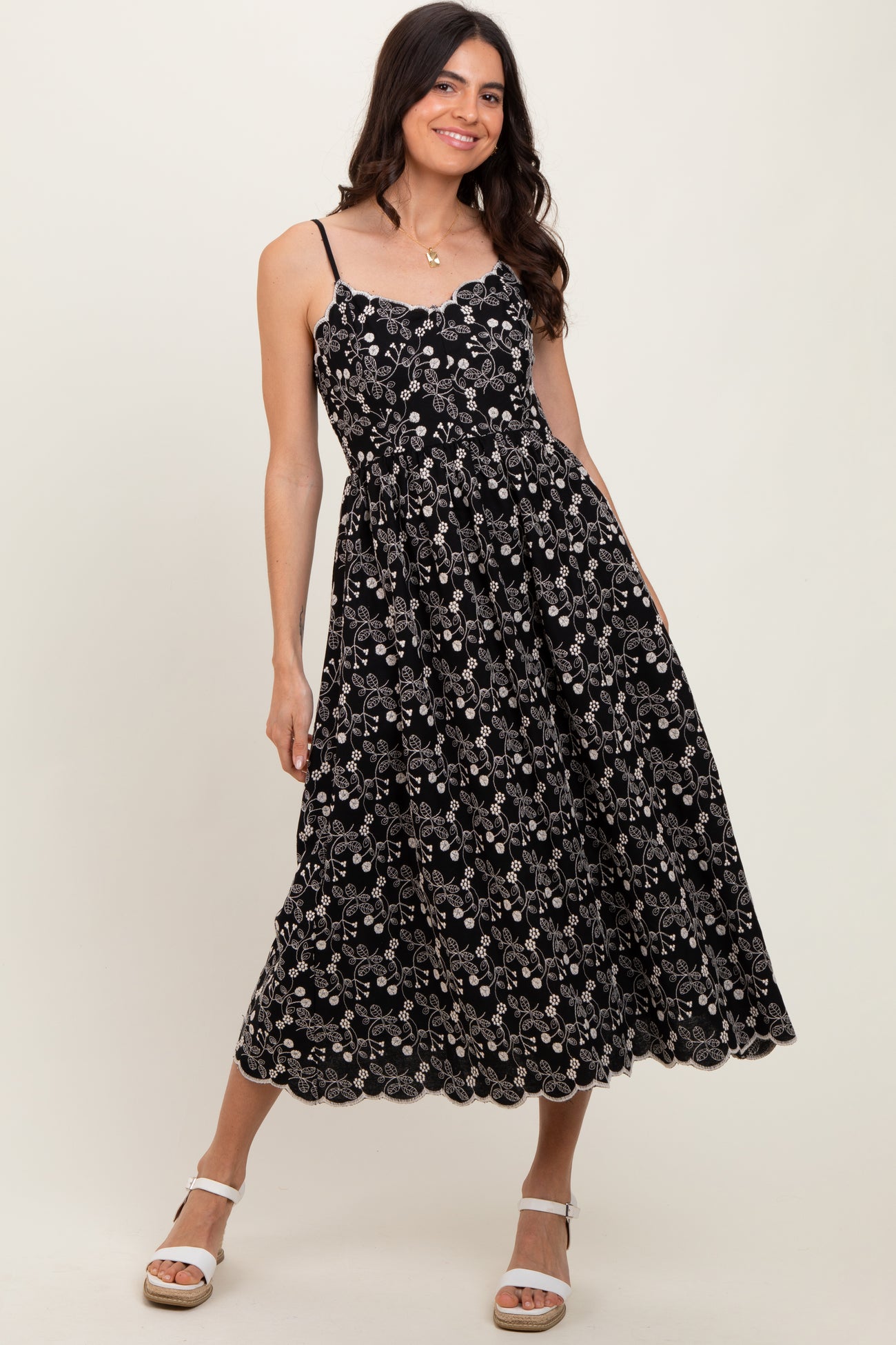 woman wearing a black floral midi dress with spaghetti straps and a scalloped hemline