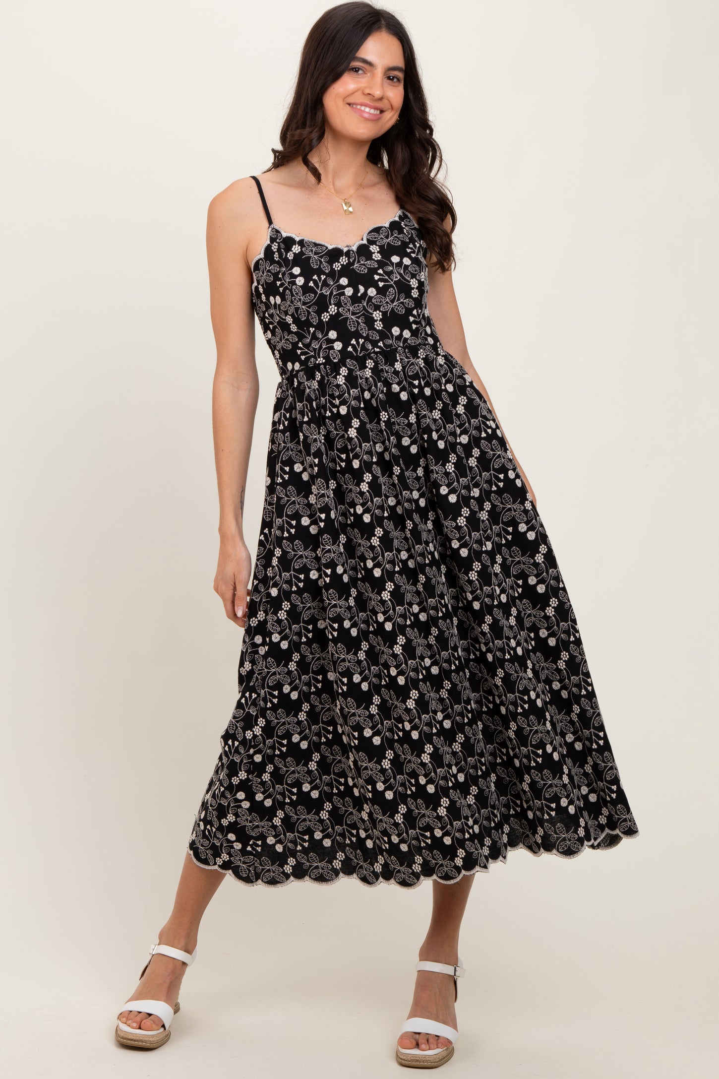 woman wearing a black floral midi dress with spaghetti straps and a scalloped hemline