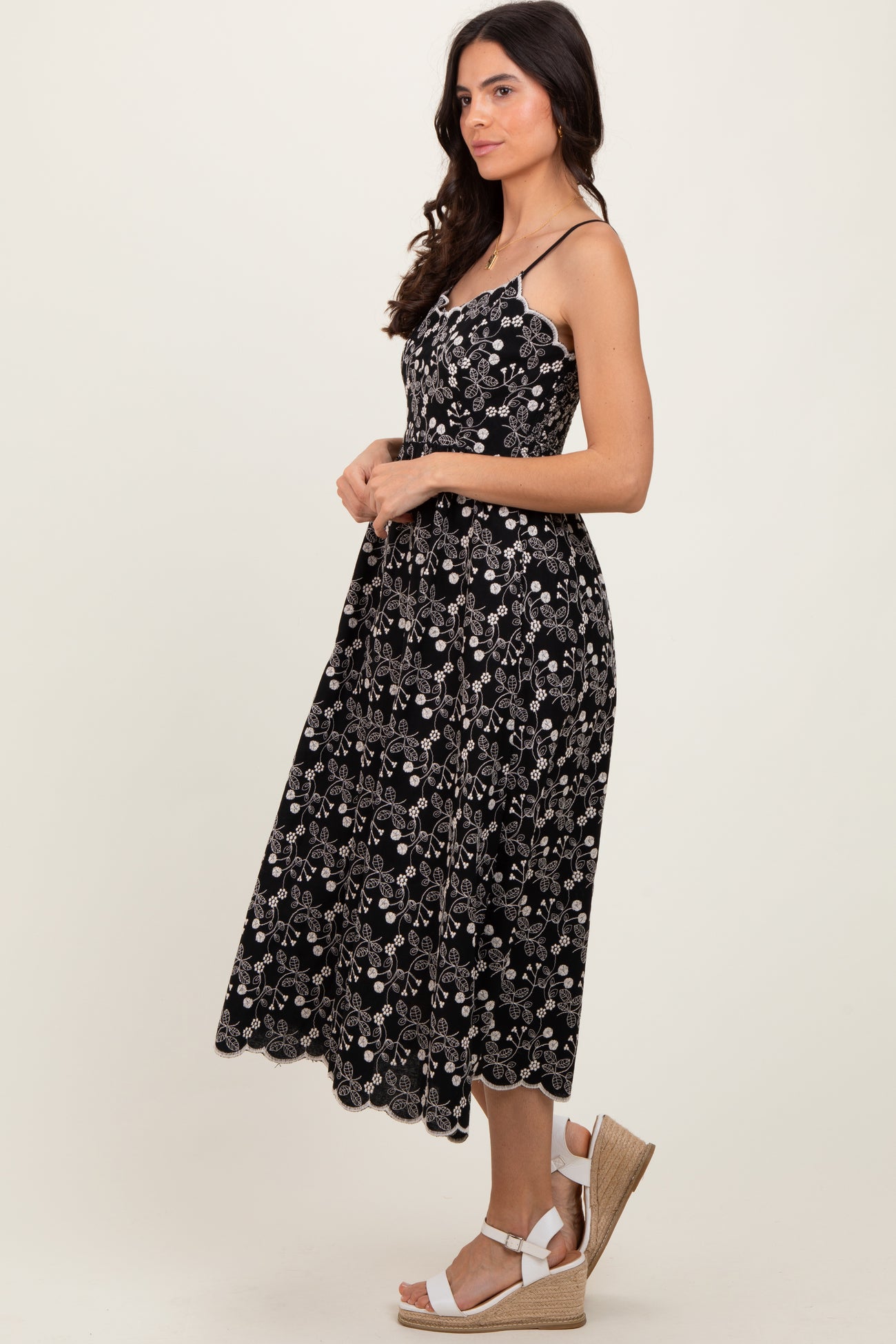 woman wearing a black floral midi dress with spaghetti straps and scalloped hem, paired with wedge sandals