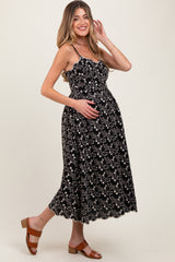 woman wearing a black floral print maternity dress with spaghetti straps and holding her baby bump