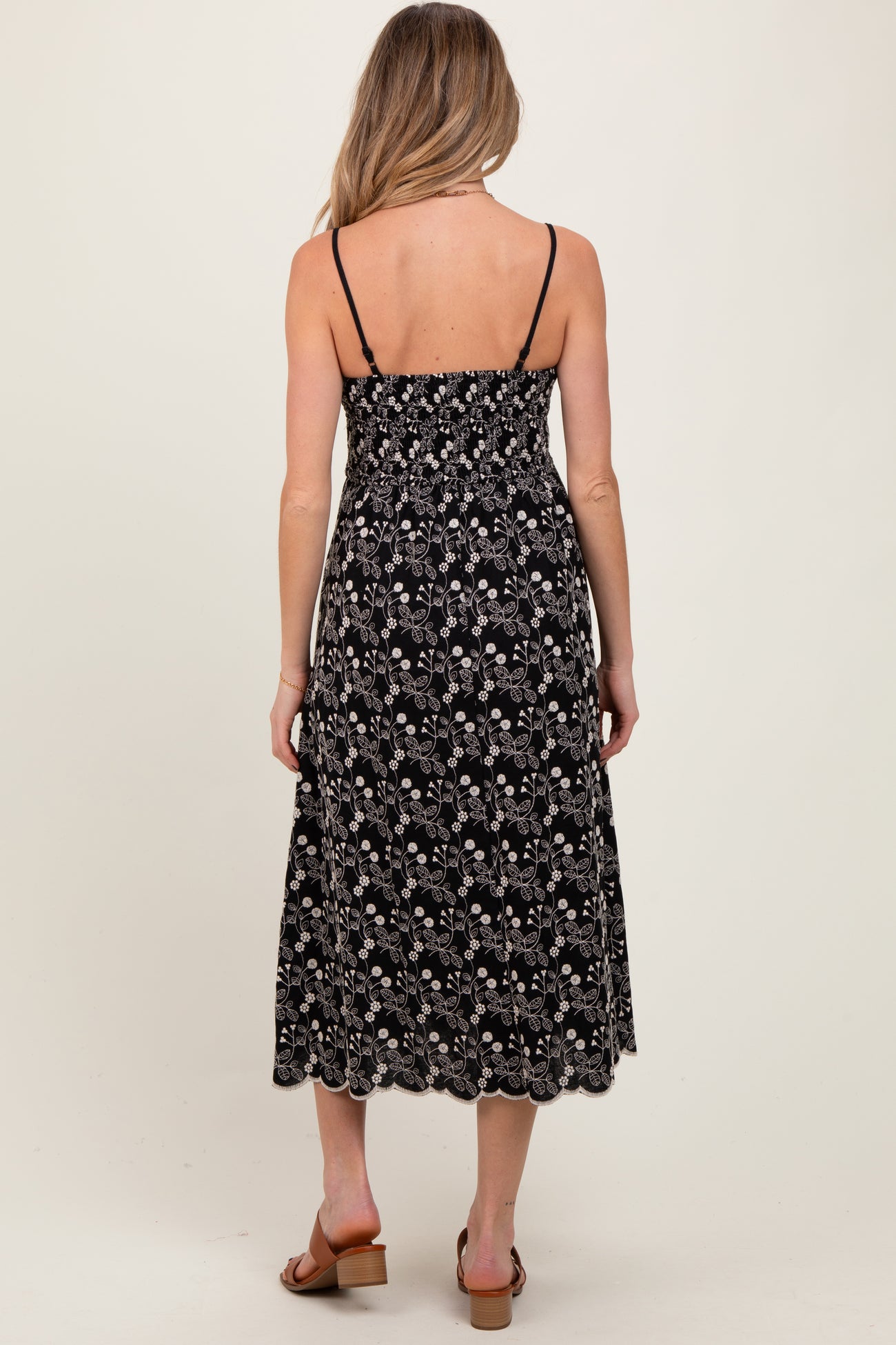 woman wearing a black floral maternity dress with adjustable straps and a smocked bodice, showing her pregnant belly