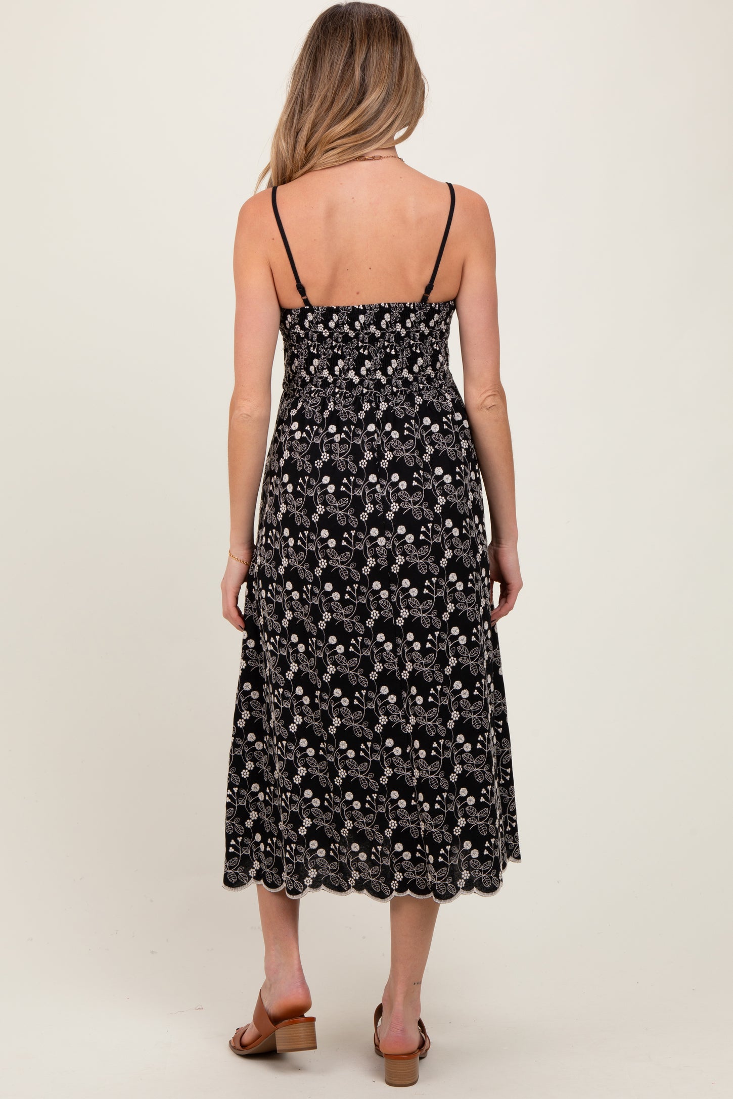 woman wearing a black floral maternity dress with adjustable straps and a smocked bodice, showing her pregnant belly
