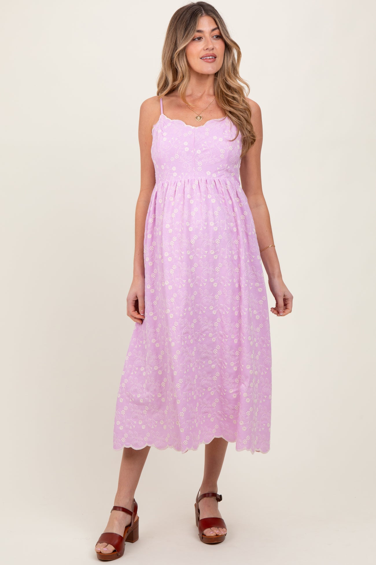 woman wearing a lavender maternity dress with scalloped hems and floral detailing, standing and smiling