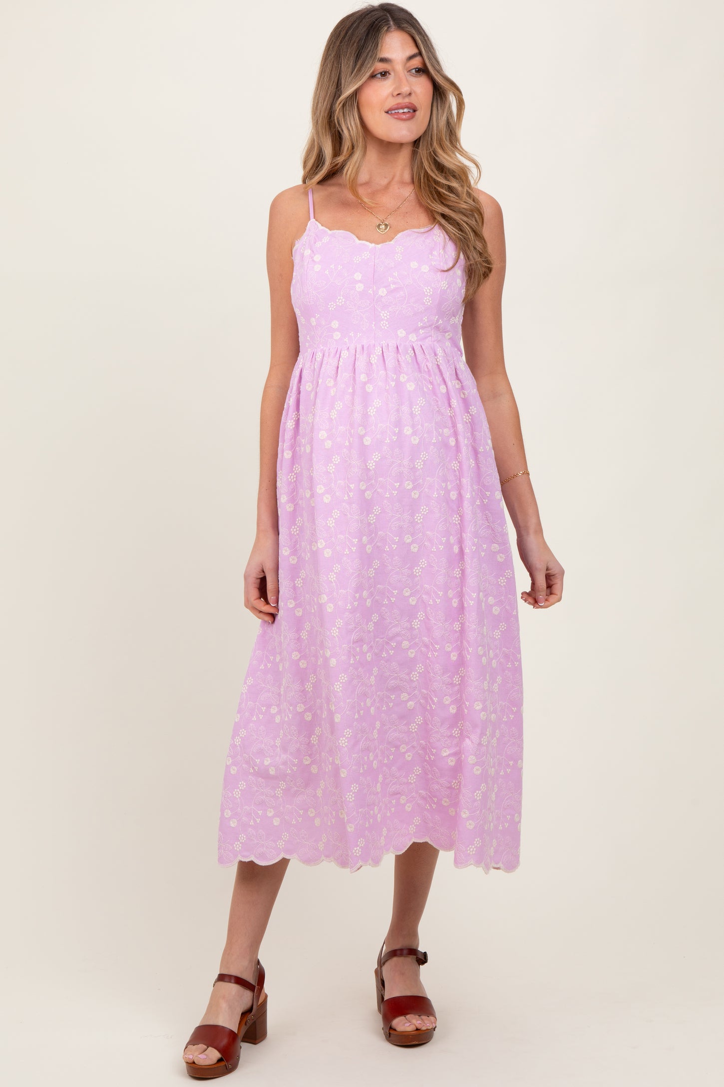 woman wearing a lavender maternity dress with scalloped hems and floral detailing, standing and smiling