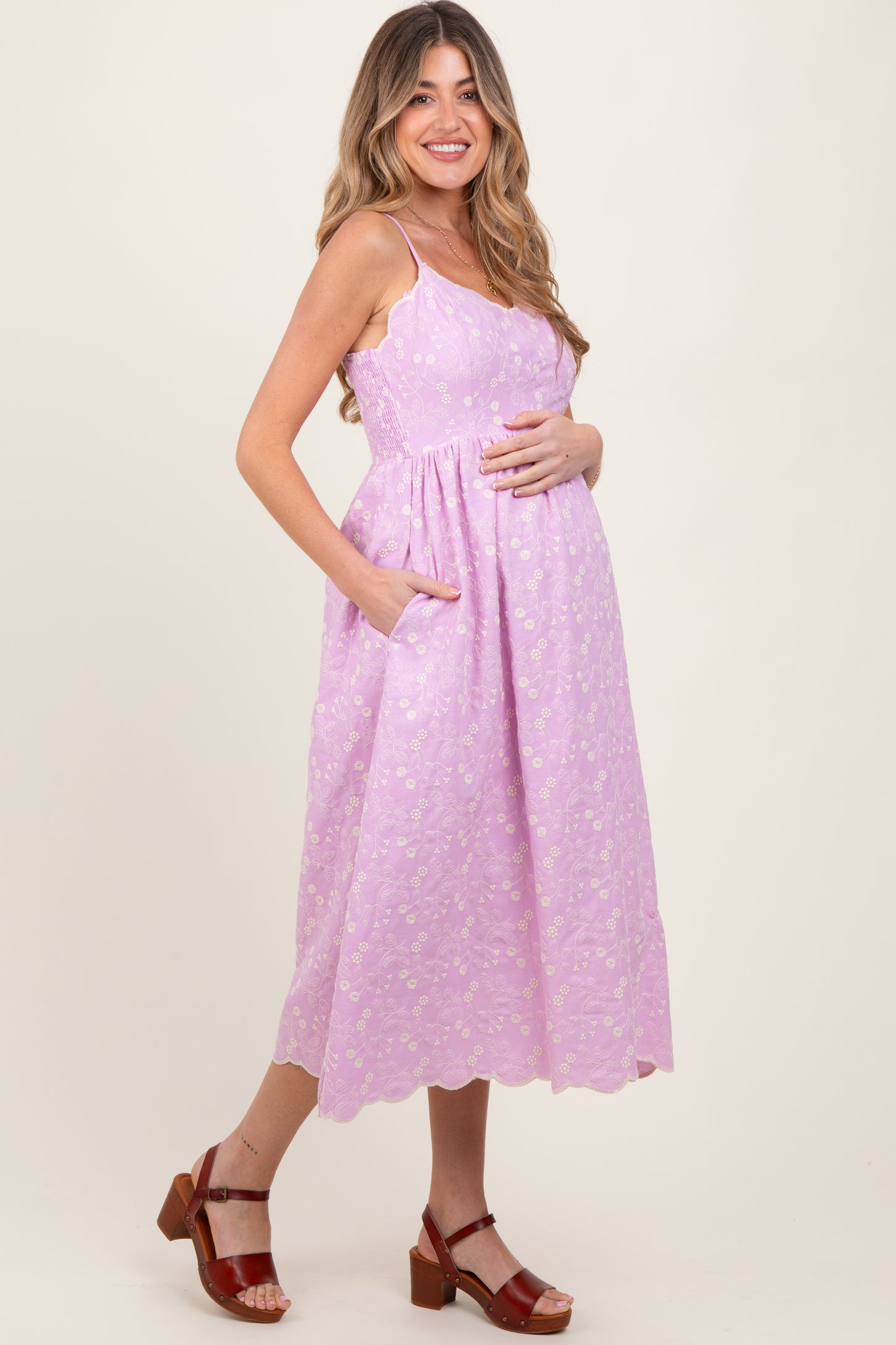 woman wearing a lavender maternity dress with floral print and pockets, holding her baby bump