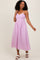 woman wearing a lilac midi dress with a scalloped neckline and floral details, styled with white sandals