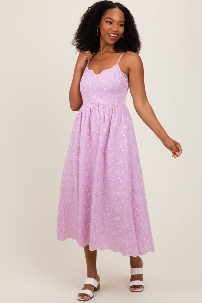 woman wearing a lilac midi dress with a scalloped neckline and floral details, styled with white sandals