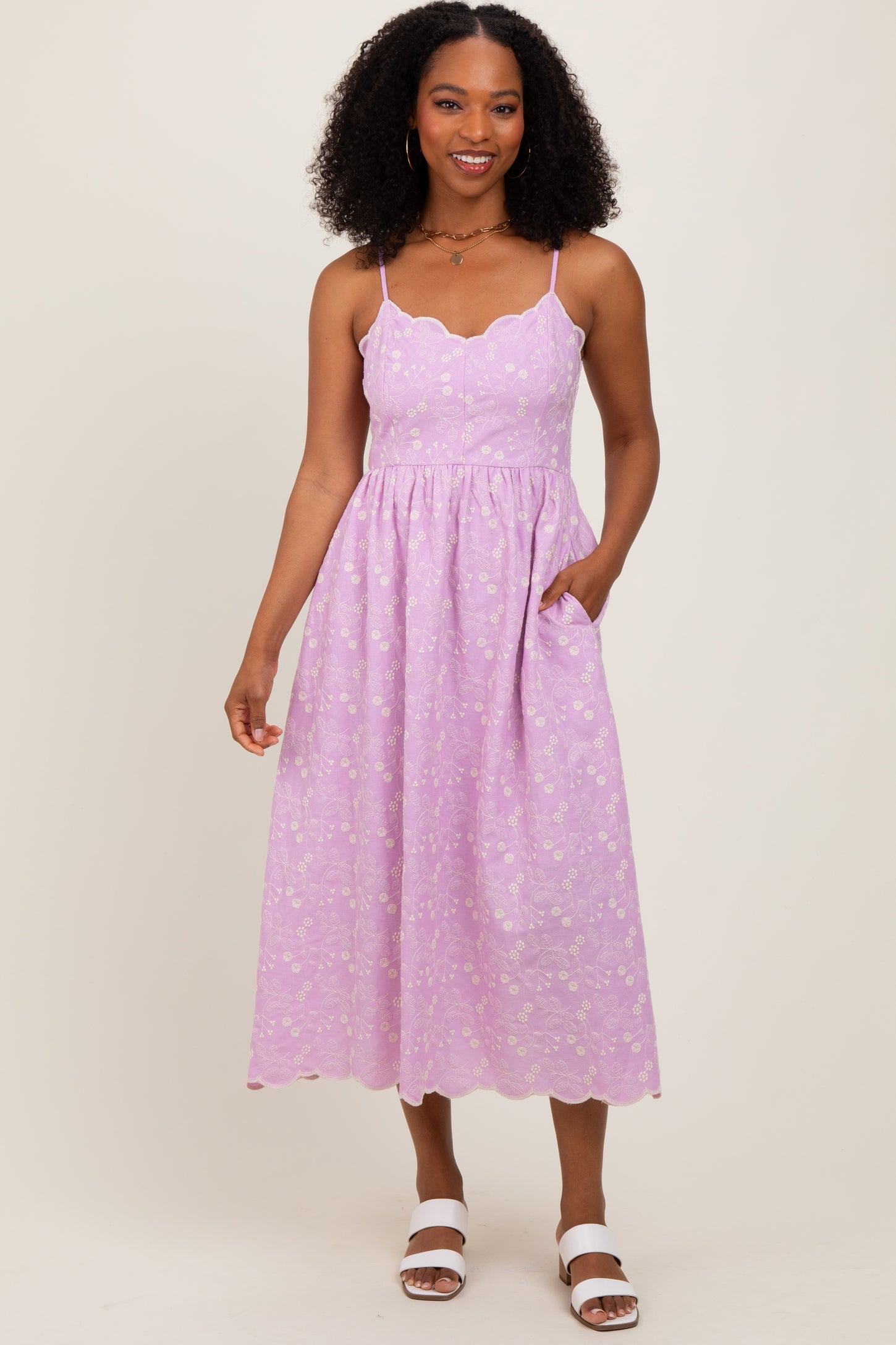 woman wearing a lavender midi dress with scalloped neckline and floral patterns, featuring pockets and spaghetti straps