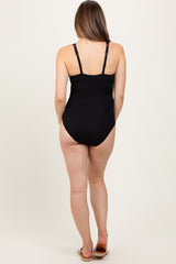 woman wearing a black ribbed maternity swimsuit, showing adjustable straps and a snug fit on her baby bump