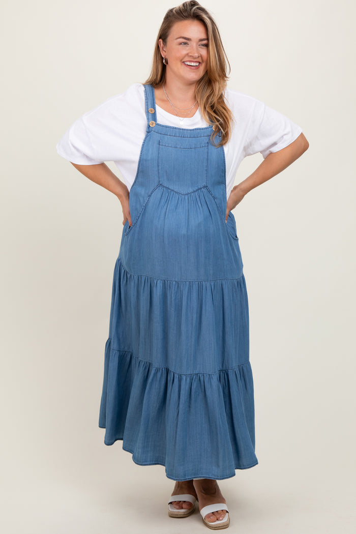 woman wearing a denim maternity plus maxi dress with tiered skirt and pockets, smiling with hands on hips
