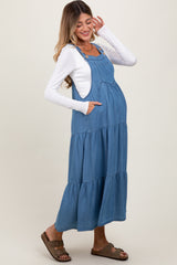 woman wearing a blue denim maternity maxi dress with tiered design and pockets, showing her baby bump