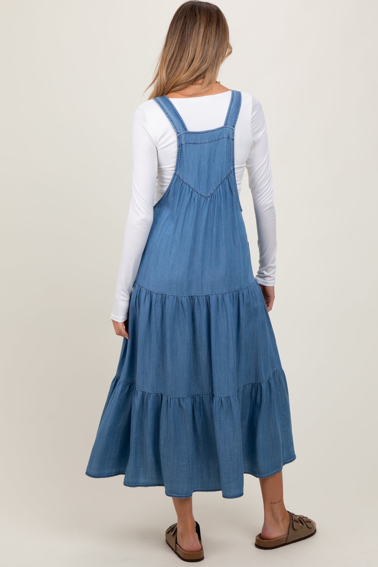 woman wearing a blue denim maternity maxi dress with tiered tiers and adjustable straps, showcasing a baby bump