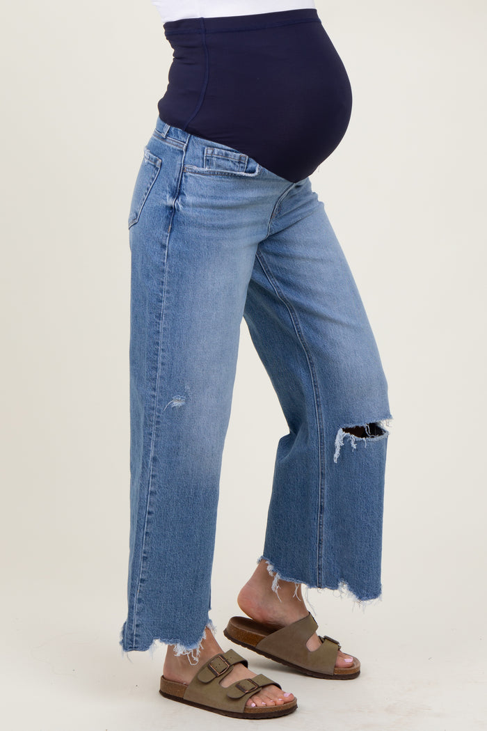 woman wearing light blue distressed maternity jeans with a navy blue over-the-bump panel and revealing her baby bump