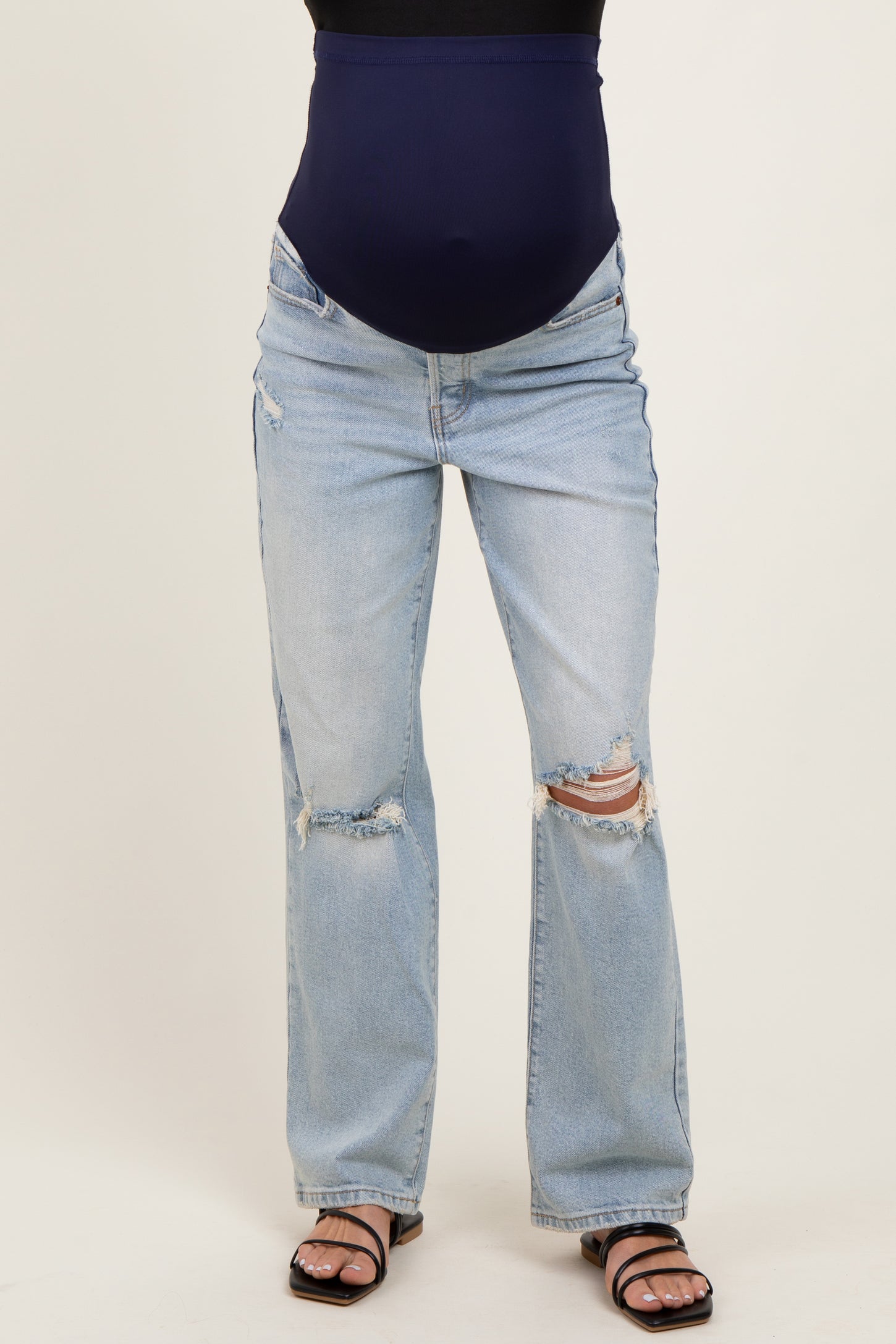 woman wearing a navy blue maternity support belly band with distressed light blue maternity jeans and black heels
