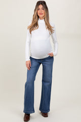 woman wearing a white long sleeve maternity top and blue flared jeans, showing her baby bump